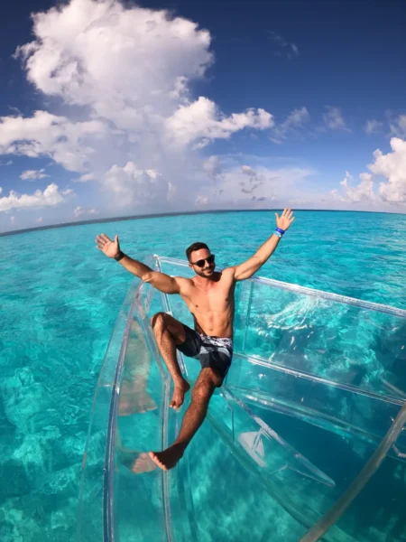Hombre sintiendo la emoción de su aventura en lancha transparente en las aguas turquesas de Isla Mujeres.