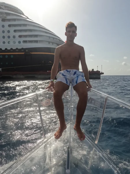 muchacho tomando el sol en el barco transparente de cozumel con el crucero de disney de fondo
