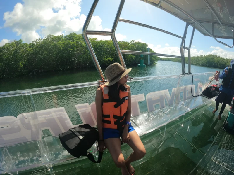 Woman with a hat on a transparent boat navigating the mangrove channels of the Nichupte Lagoon in Cancun.