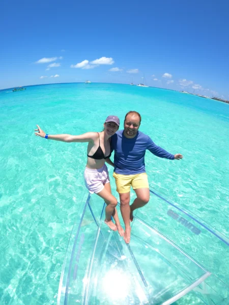 A happy couple laughing and enjoying the view from a 100% transparent boat on the crystal-clear turquoise waters of Isla Mujeres, Mexico.