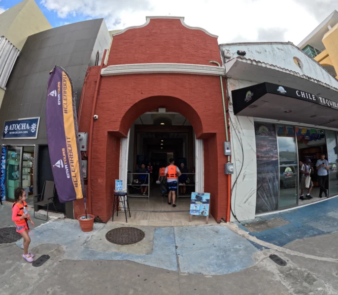 Fachada de la oficina de Transparent Boat Tours Cozumel en la Avenida Melgar, con clientes y niños listos para comenzar su tour. Fachada color naranja con arco de la oficina barco transparente Cozumel ubicada en la avenida principal.