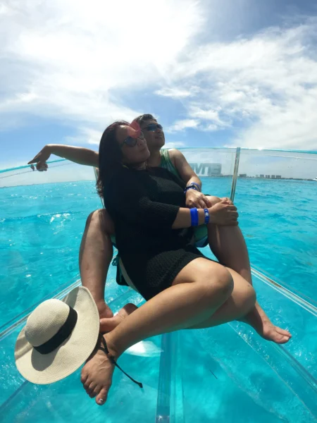 Vistas Inolvidables: El Mejor Tour de Cancún 4 Pareja relajándose abrazada en la proa de un barco transparente cancún sobre el brillante mar turquesa de la rivera maya, disfrutando de un momento juntos.