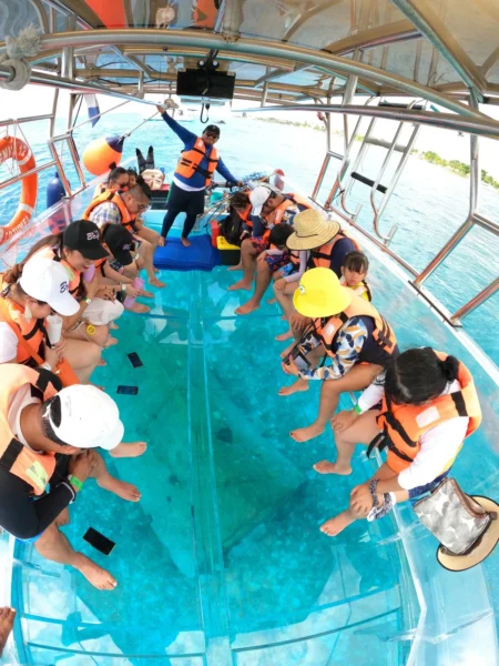 Grupo de turistas con chalecos salvavidas sentados en una lancha 100% transparente, observando el arrecife y los peces de Cozumel directamente a través del suelo de cristal.