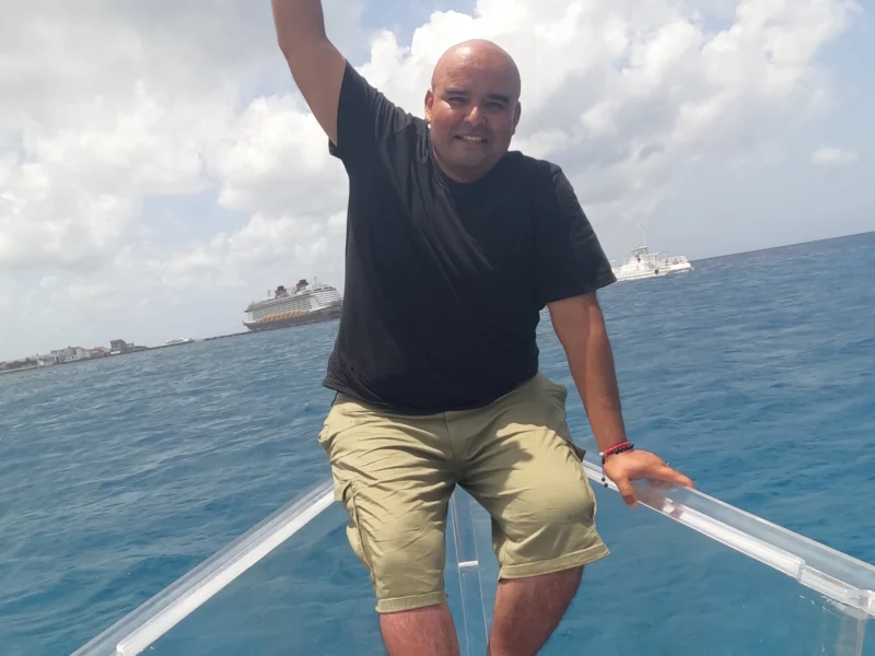 Smiling man enjoying a clear boat tour in Cozumel, Mexico, over turquoise Caribbean waters with glass-bottom view.