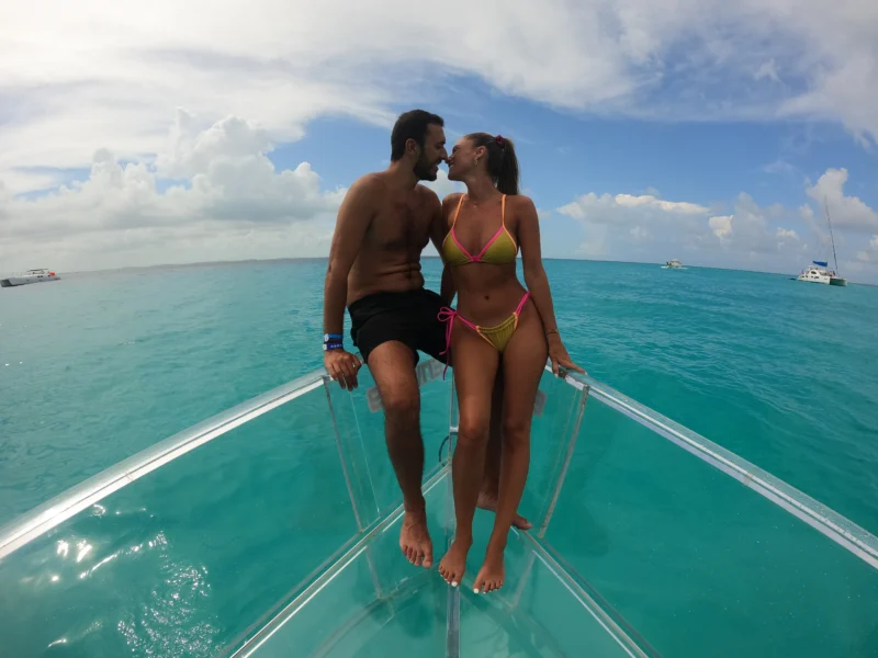 A loving couple about to kiss on the bow of a 100% transparent boat, enjoying a romantic tour on the beautiful turquoise waters of Isla Mujeres.