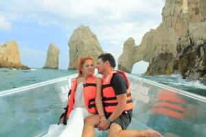 Pareja disfrutando un momento romántico en una lancha transparente con el famoso Arco de Cabo San Lucas de fondo durante un tour en Los Cabos