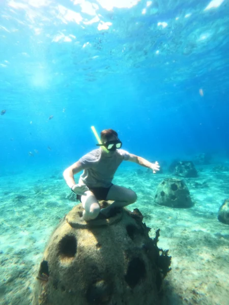 Man enjoying a snorkeling adventure in the clear turquoise water, exploring an underwater reef structure during a stop on a clear boat Cozumel tour.