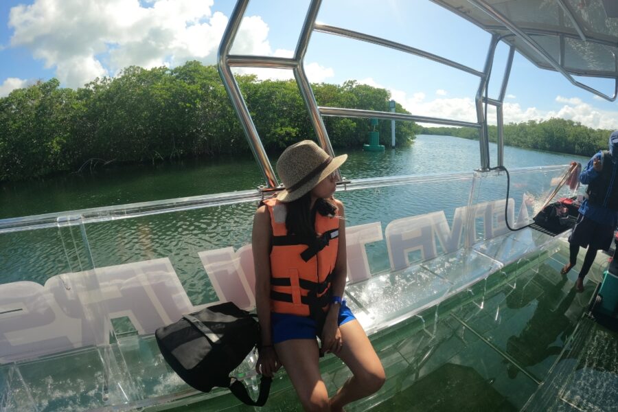 Tourist enjoying the scenic view of Nichupte Lagoon mangroves from a transparent boat in Cancun. Calm green waters and nature observation.