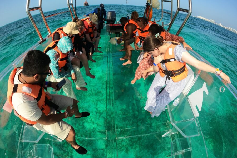 Group of tourists on a transparent boat looking down at the Blanquizal reef area in Cancun. The water is turquoise and clear.