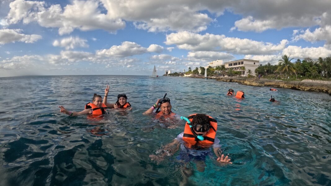 Small group of tourists enjoying a guided snorkeling adventure in the shallow turquoise waters of Cozumel near the shoreline.