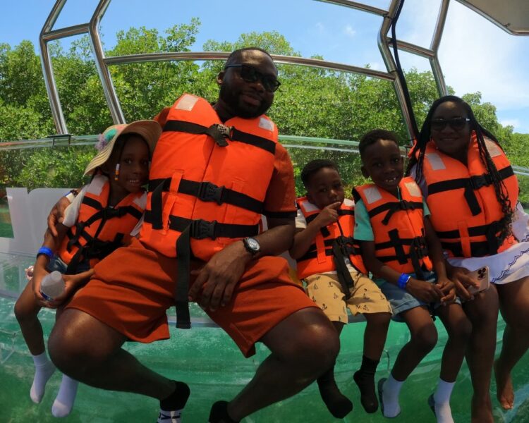 Tourists enjoying the view of Cancun's marine life and reefs through the glass bottom of a transparent boat.