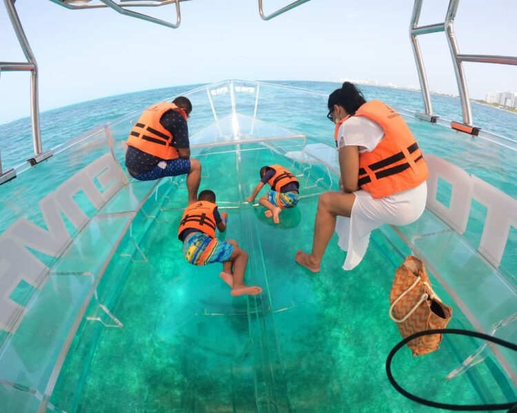 A family with children in life jackets looking through the glass floor of a transparent boat in the turquoise waters of Cancun, optimized for Caribbean boat tours World Cup 2026.