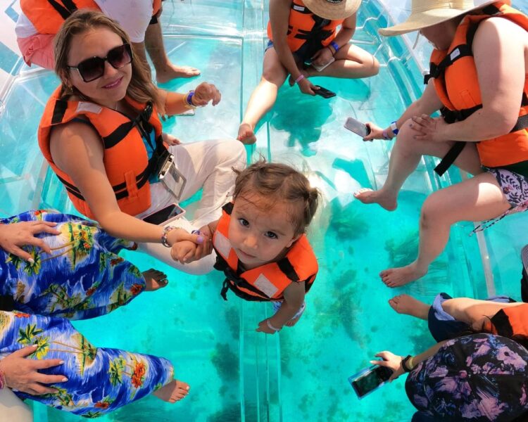 A young girl and her family looking through the glass floor of a transparent boat in the shallow waters of Isla Mujeres, optimized for Caribbean boat tours World Cup 2026.