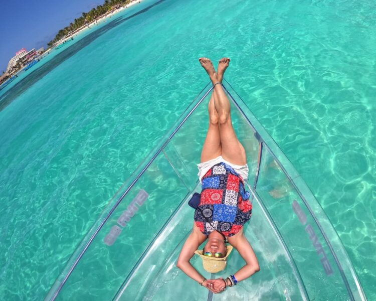 An overhead view of a woman relaxing on the bow of a transparent boat in the bright turquoise waters of Isla Mujeres, optimized for Isla Mujeres World Cup 2026.