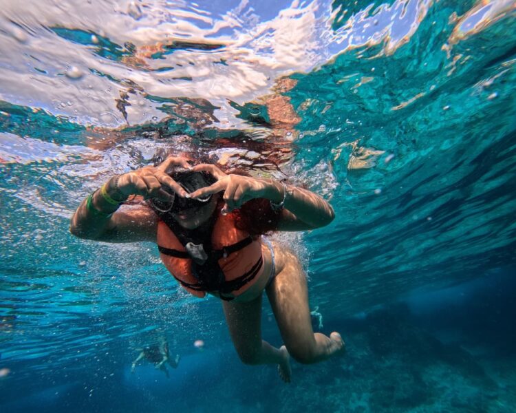 Tourist snorkeling and making a heart gesture in the clear waters of Cozumel during a transparent boat tour for FIFA World Cup 2026 visitors.